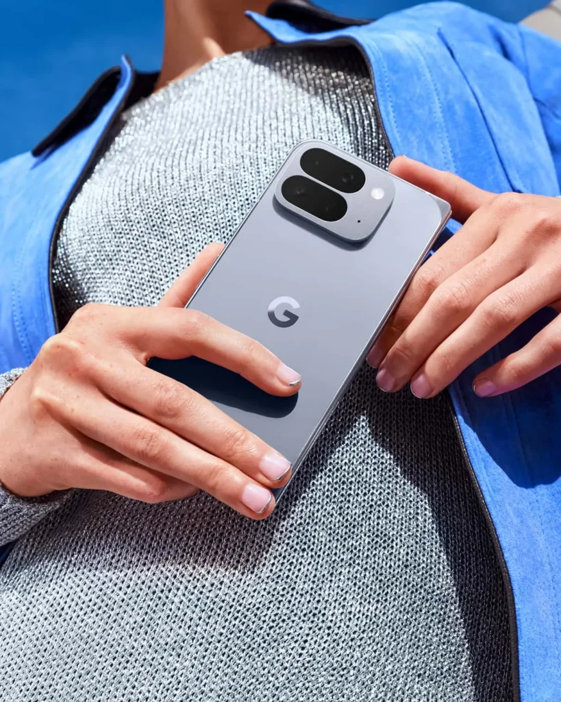 Google Pixel 10 Pro Fold, in Moonstone, held in hands against blue clothing