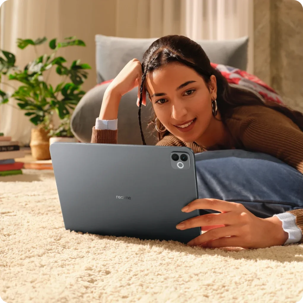 realme Pad 3, in Space Grey, held by a woman lying on a rug