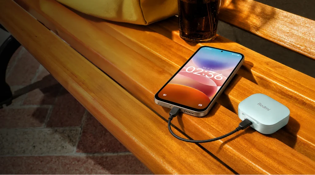Xiaomi Redmi 17 5G, charging earbuds by cable on a wooden bench