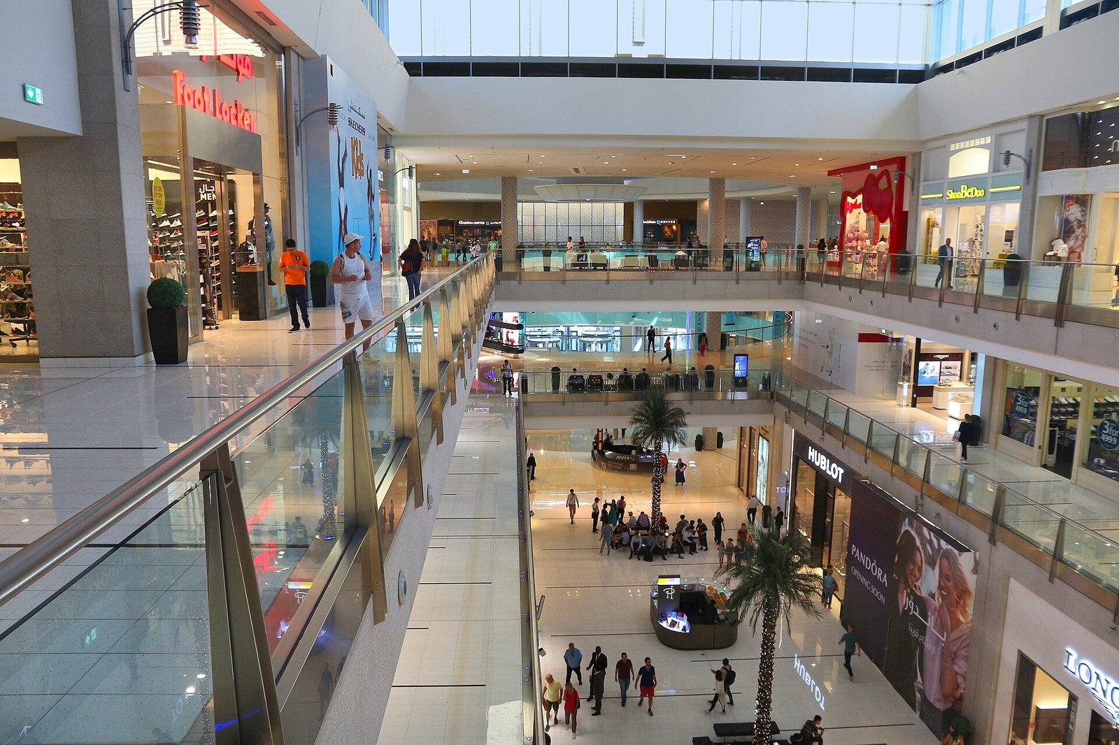 Shoppers on the upper floors of a Dubai mall, with palm trees in the atrium