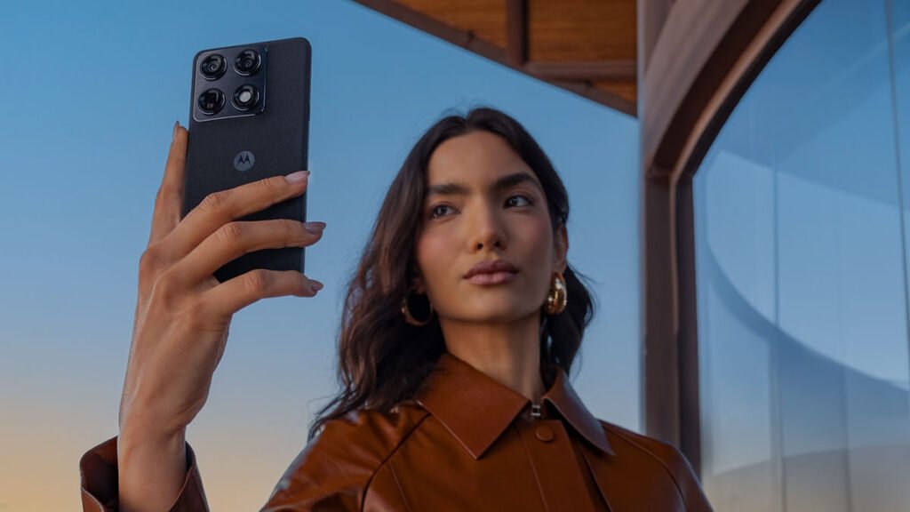 A woman holds up a black Motorola Signature, showing the four-lens camera block on its back, against a dusk sky
