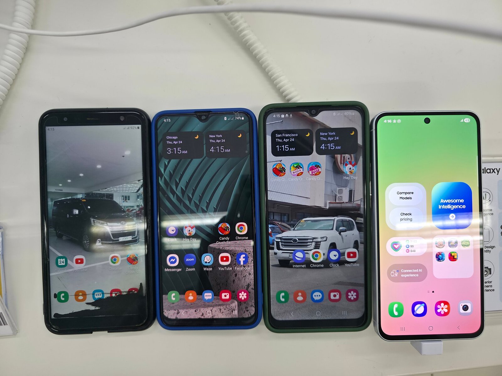 Four Samsung phones lined up on a shop counter, from an older Galaxy J4+ on the left to a Galaxy A56 5G on the right