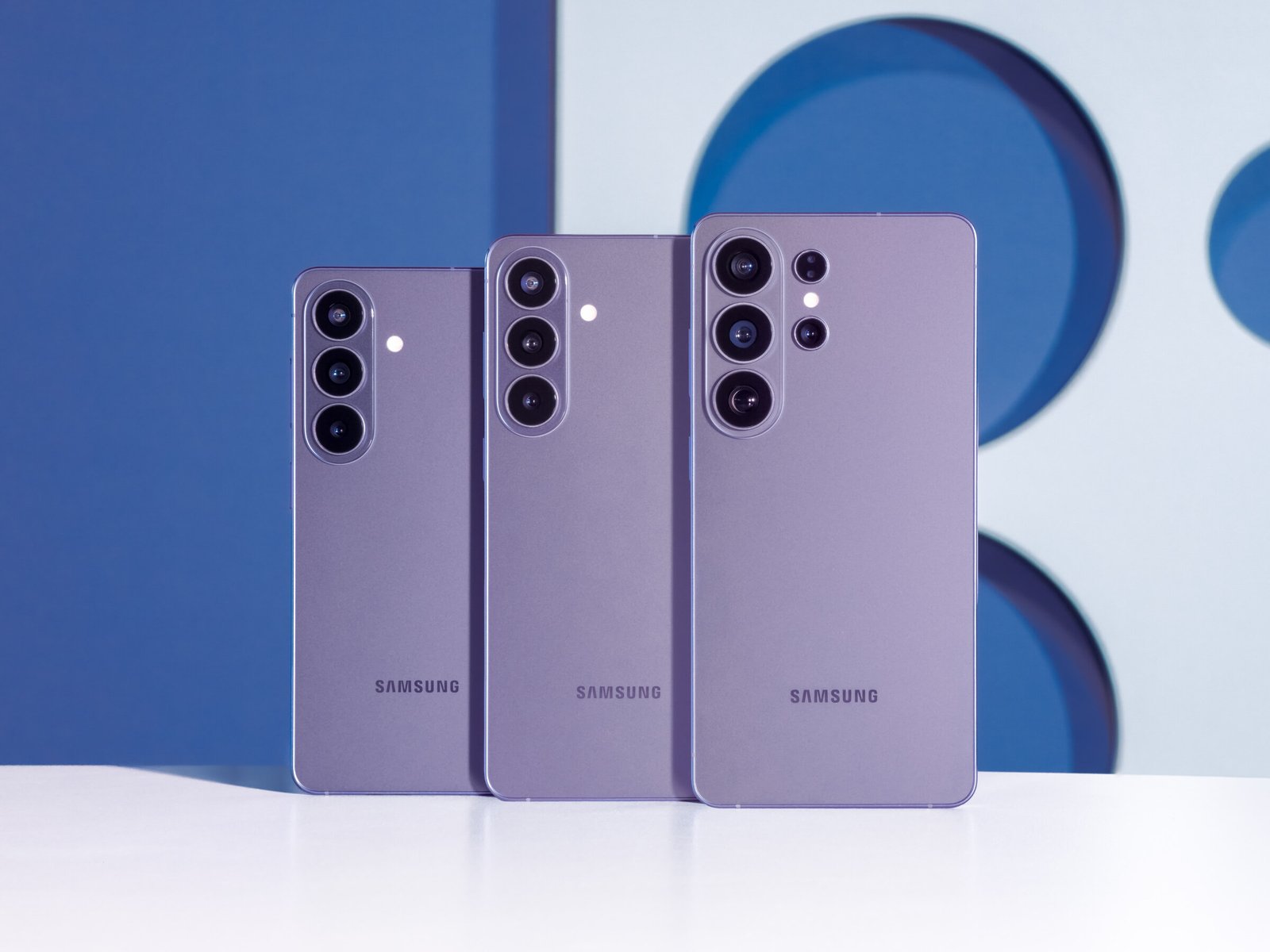 Samsung Galaxy S26, Galaxy S26+ and Galaxy S26 Ultra standing side by side in purple against a blue backdrop