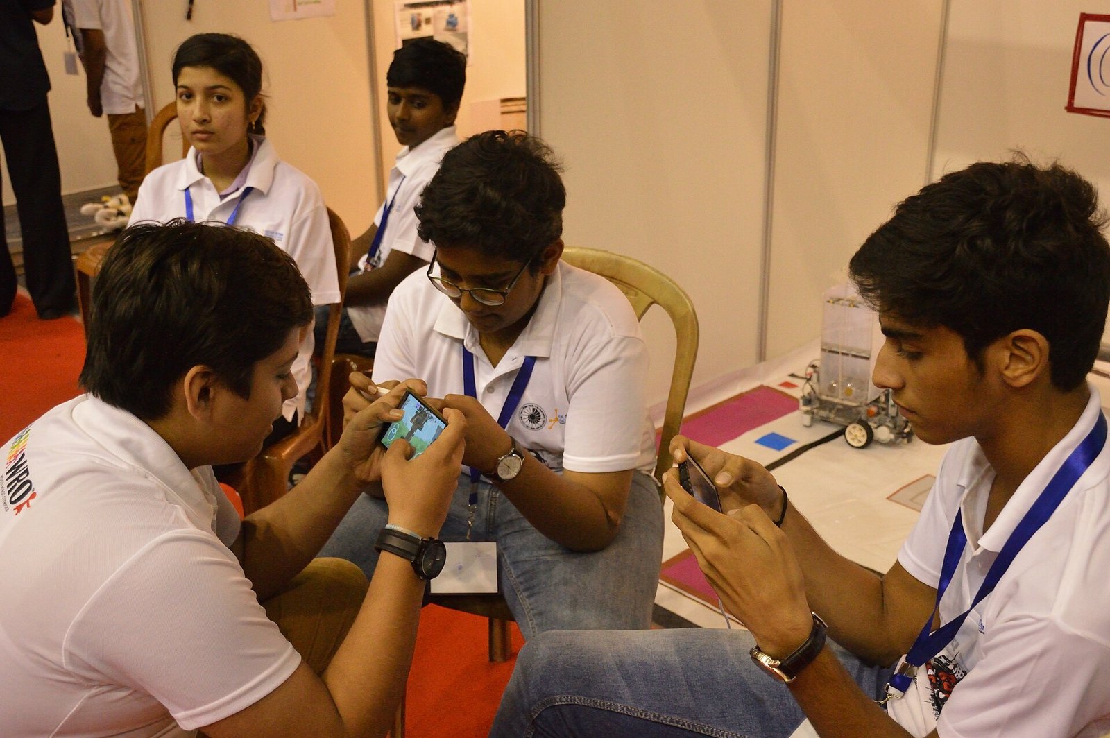 Students in white polo shirts playing a game on their phones at a robotics event in Kolkata